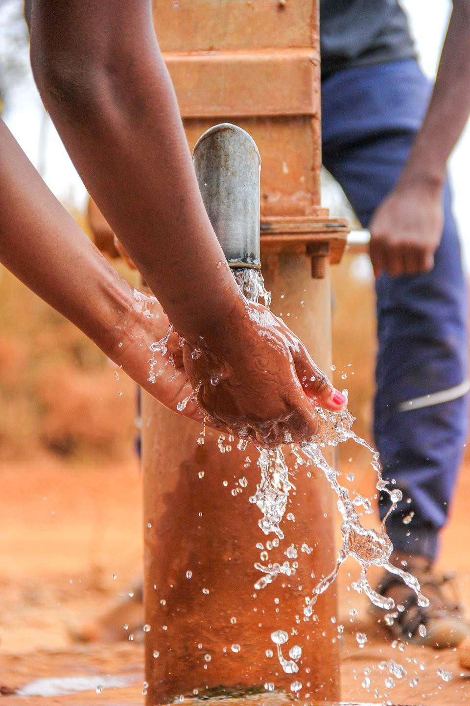Hands being washed under water flowing from a rural pump.