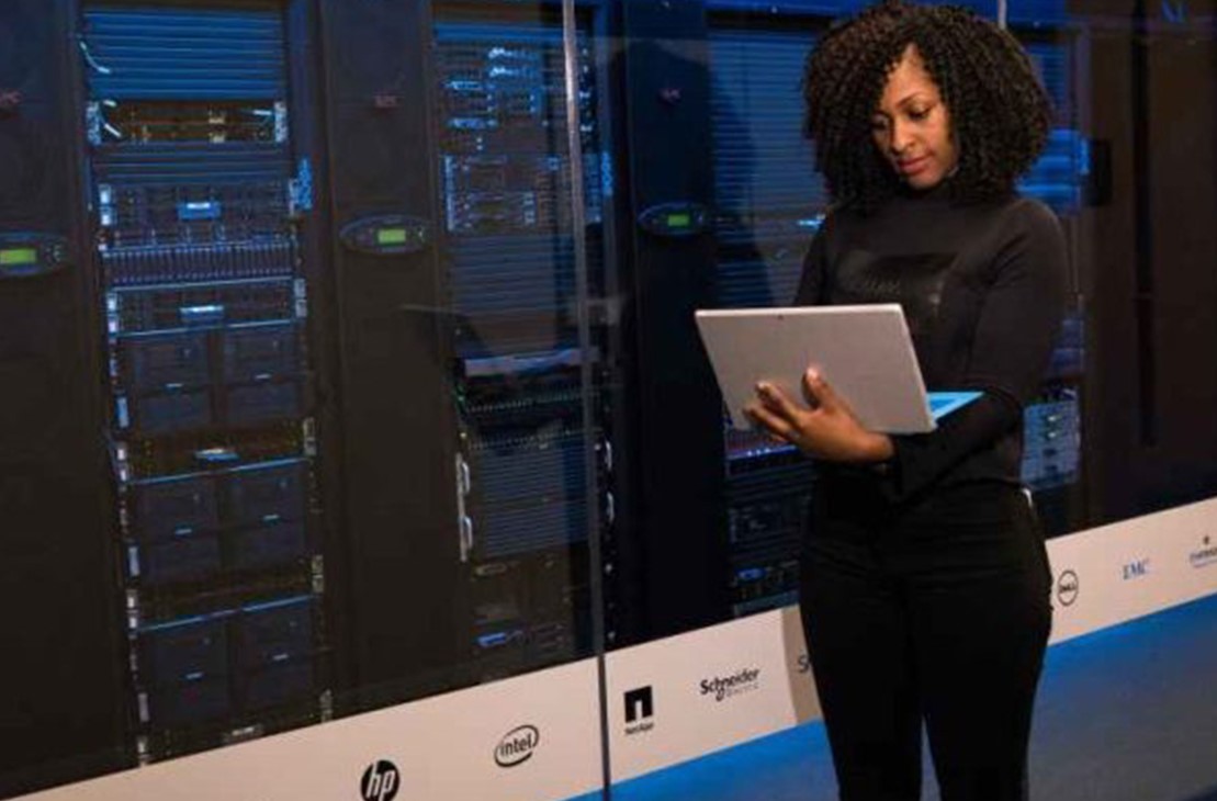 A woman using a laptop beside server racks in a data centre.