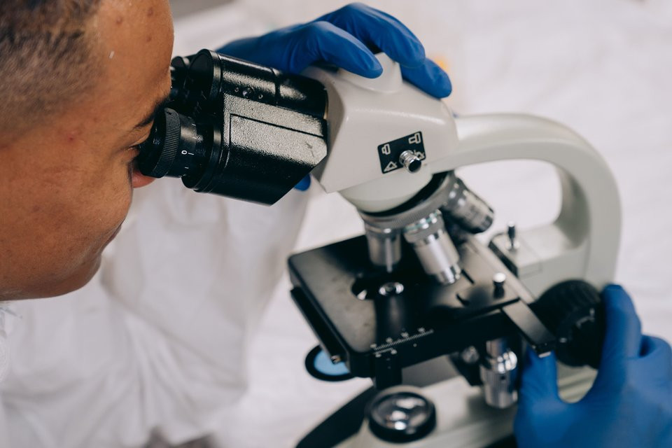 A Black laboratory scientist examines a sample using a microscope.