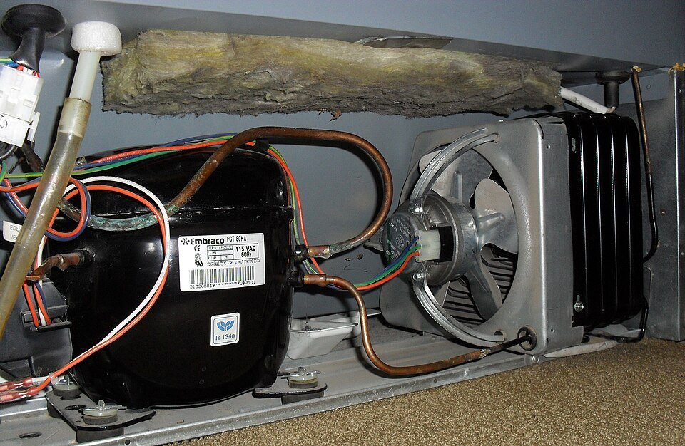 A refrigeration compressor, copper pipework, cooling fan and condenser coil exposed for inspection.