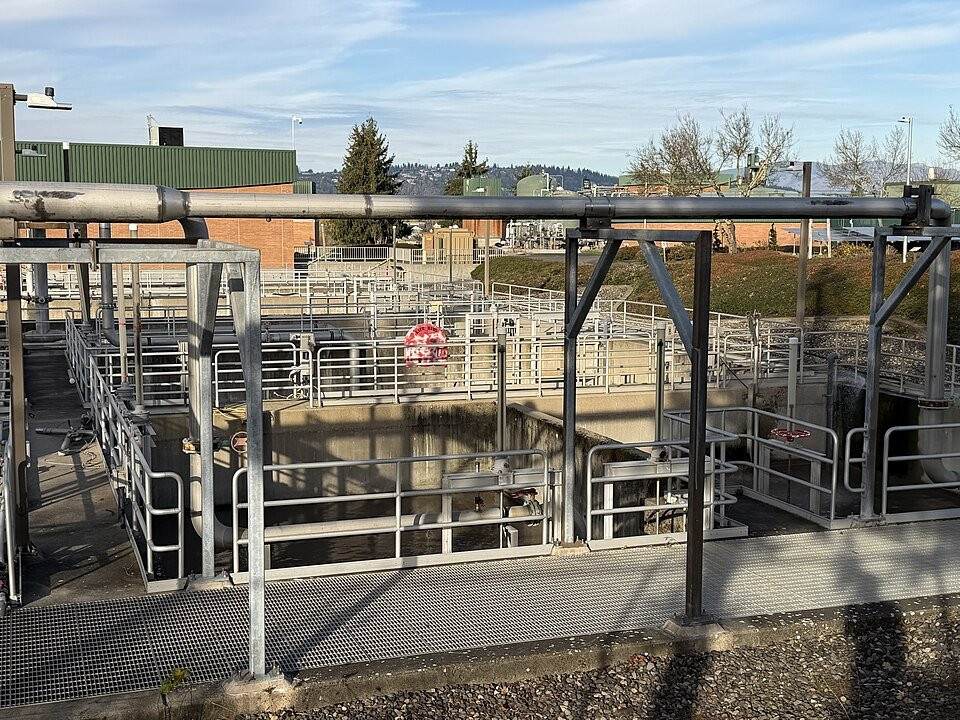 Clarifier tanks, pipework and protected walkways at a wastewater treatment plant.