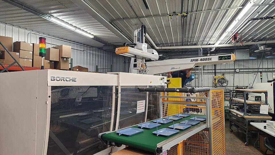 Industrial injection moulding machine with a robotic handling arm for plastics processing.