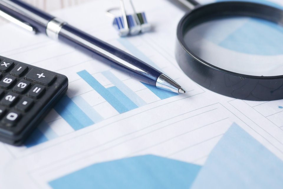 Magnifying glass, calculator and pen on financial records, illustrating the examination of financial evidence.
