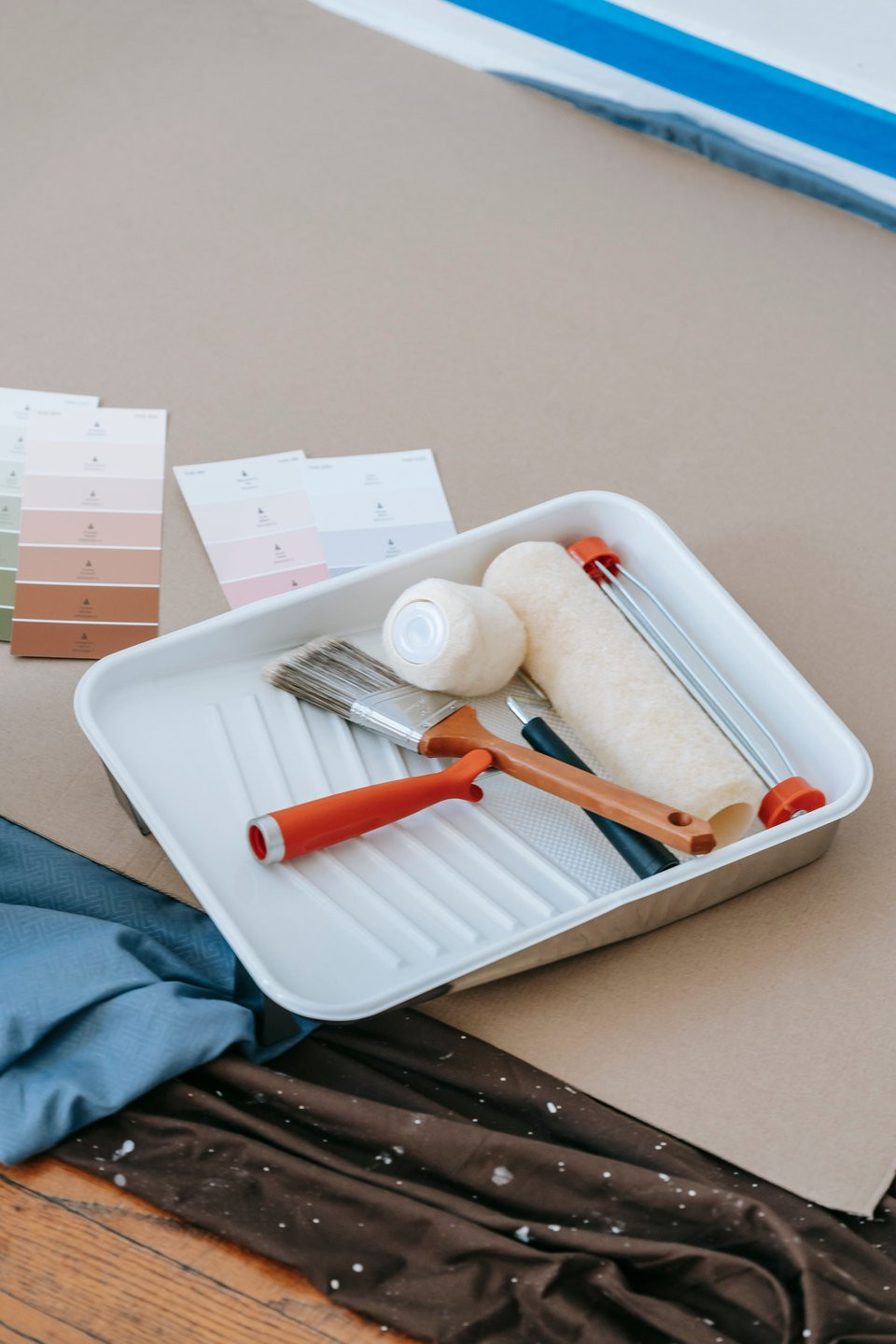 Paint rollers and brushes in a tray beside colour swatches.