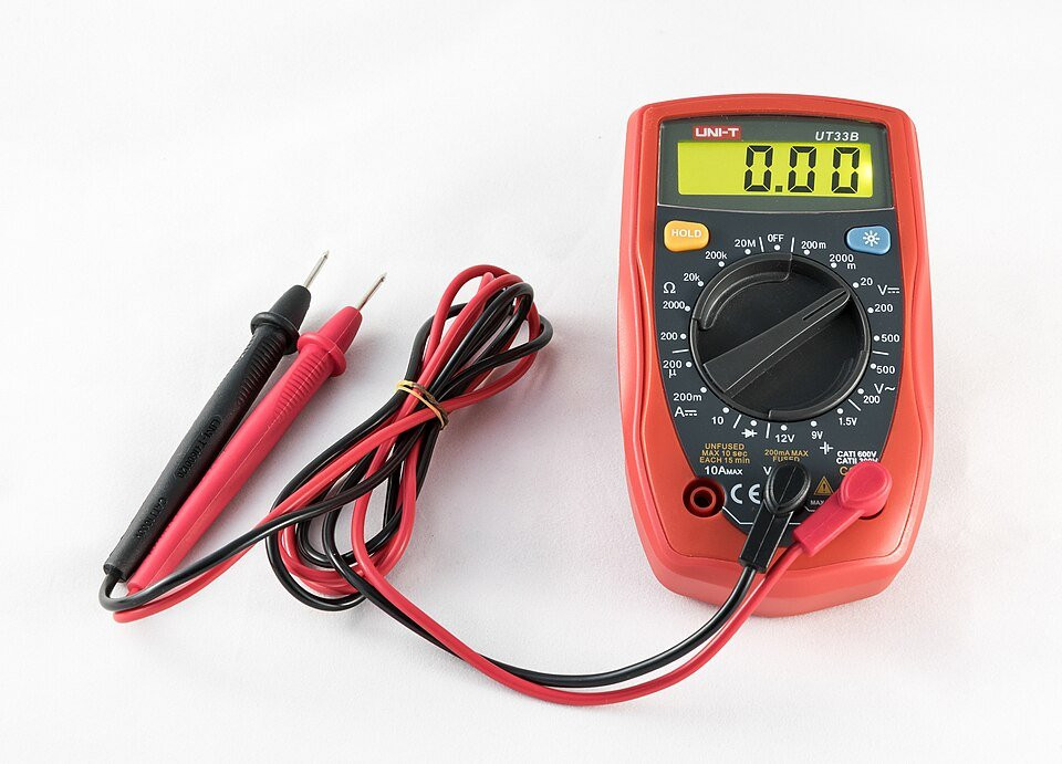 A digital multimeter with red and black probes on a white surface.