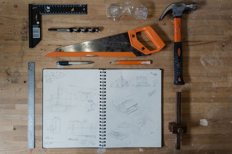 Technical sketches, measuring tools, a saw and safety glasses on a workbench.