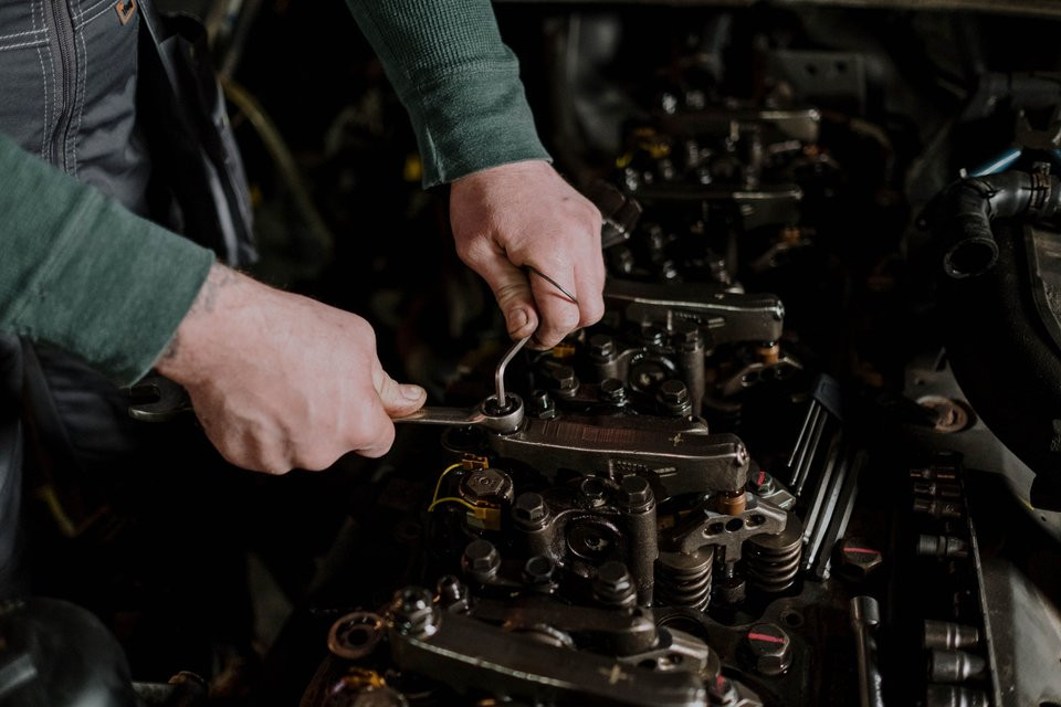 Mechanic adjusting an exposed diesel engine valve assembly with hand tools.
