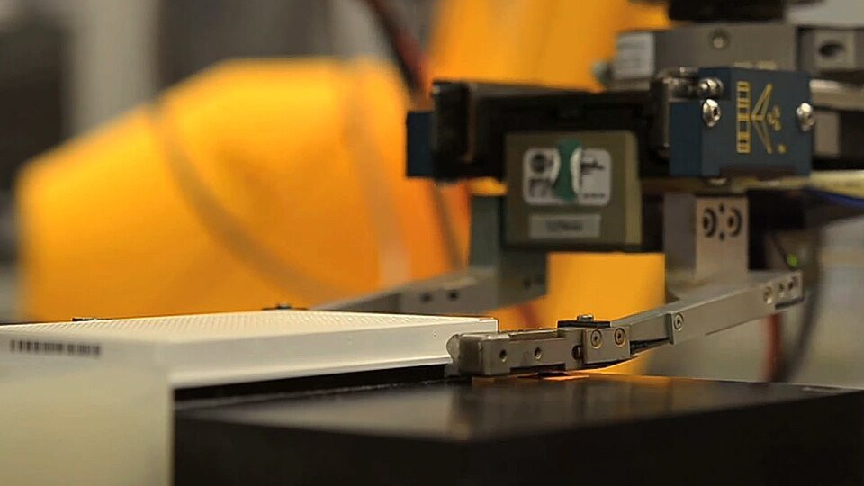 Robot gripper transferring a laboratory assay plate, illustrating mechatronic control and automated handling.